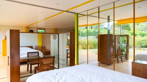 Floor to ceiling wardrobes run full length of bed. At the foot of the bed is a glass dressing table surrounded by mirrors.